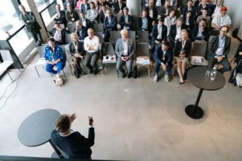 Menschen sitzen im Publikum, Mann spricht vorne